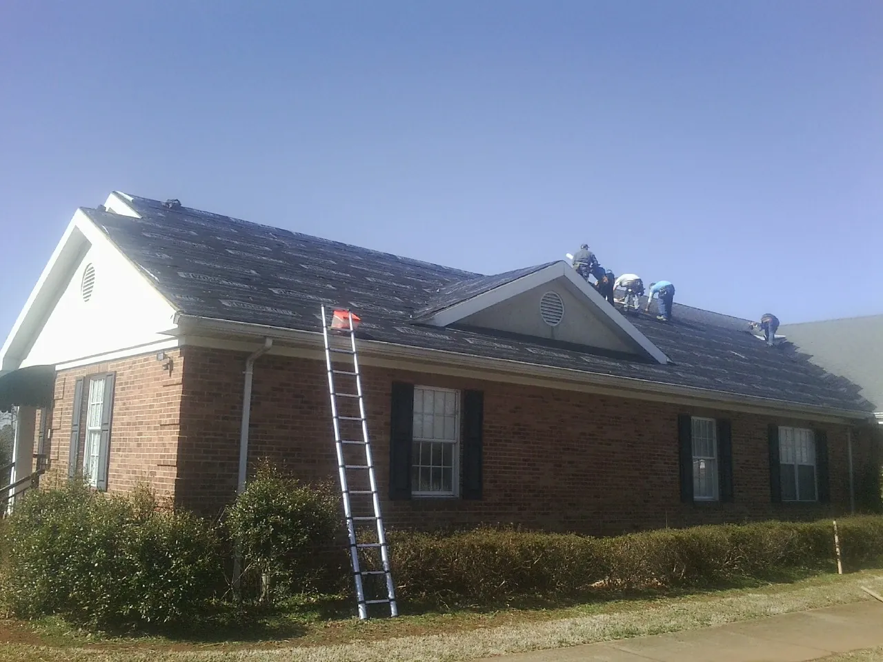 Crew tearing shingles off a brick ranch roof with a ladder set — Emergency Roof Repair work by our crew in Ipswich