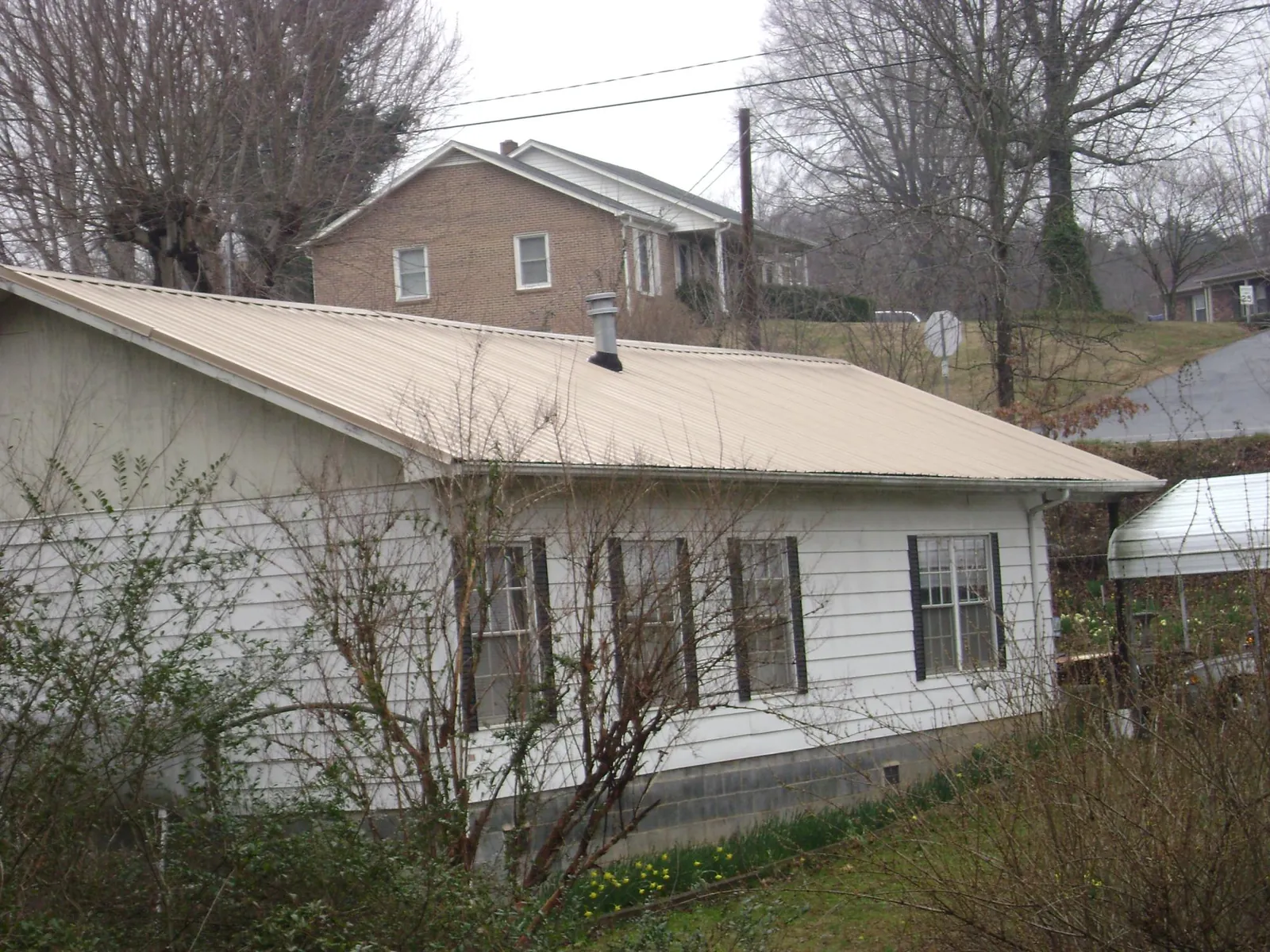 Tan metal roof on a white sided house set into a hillside — Commercial Roofing by Roofing Brothers in Ipswich