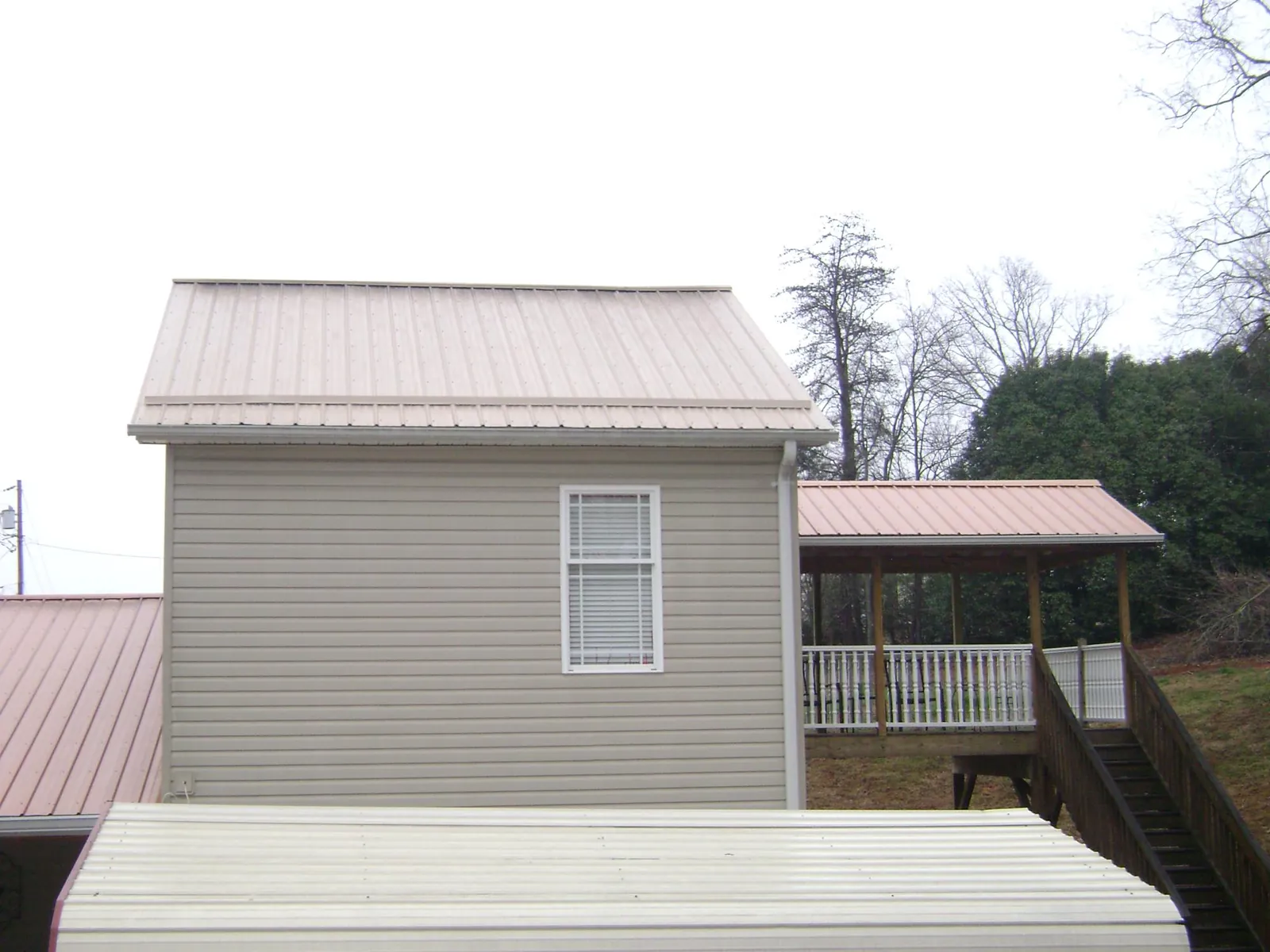 Tan metal roofs on a two story addition and attached porch, from a Roof Replacement job in Ipswich